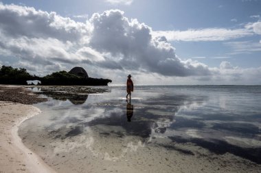Mavi şapkalı kadın denizin alçak gelgiti sırasında mercan ve adaların arka planına poz veriyor. 
