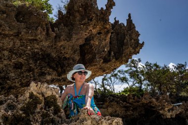Mavi şapkalı kadın denizin alçak gelgiti sırasında mercan ve adaların arka planına poz veriyor. 