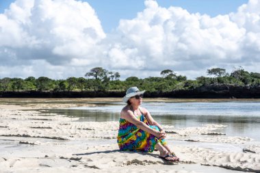 Mavi şapkalı kadın denizin alçak gelgiti sırasında mercan ve adaların arka planına poz veriyor. 
