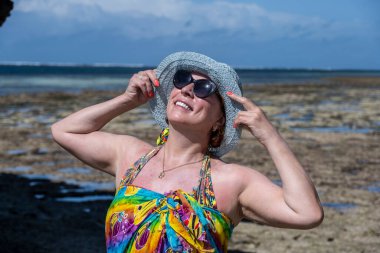 Mavi şapkalı kadın denizin alçak gelgiti sırasında mercan ve adaların arka planına poz veriyor. 