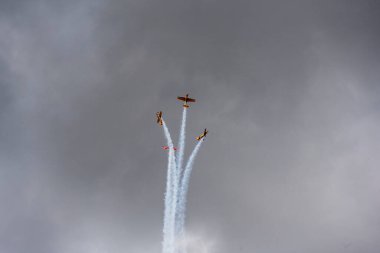 a group of combat aircraft perform complex aerobatics with a smoke launch against the sky