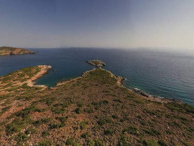 Deniz ve dağların panoramik görüntüsü ve bir drondan çekilen turkuaz su üzerindeki gemiler.