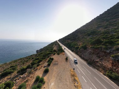 Deniz ve dağların panoramik görüntüsü ve bir drondan çekilen turkuaz su üzerindeki gemiler.