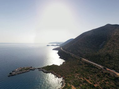 Deniz ve dağların panoramik görüntüsü ve bir drondan çekilen turkuaz su üzerindeki gemiler.