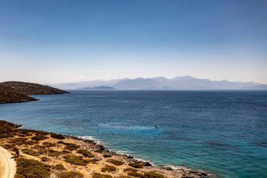 Deniz ve dağların panoramik görüntüsü ve bir drondan çekilen turkuaz su üzerindeki gemiler.