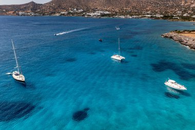 Deniz ve dağların panoramik görüntüsü ve bir drondan çekilen turkuaz su üzerindeki gemiler.