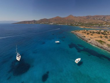 Deniz ve dağların panoramik görüntüsü ve bir drondan çekilen turkuaz su üzerindeki gemiler.
