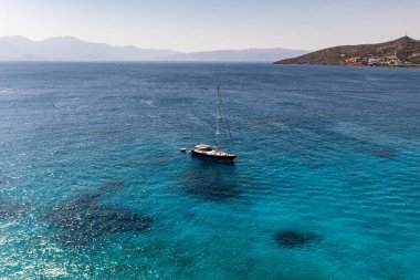 Deniz ve dağların panoramik görüntüsü ve bir drondan çekilen turkuaz su üzerindeki gemiler.