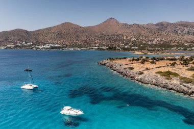 Deniz ve dağların panoramik görüntüsü ve bir drondan çekilen turkuaz su üzerindeki gemiler.