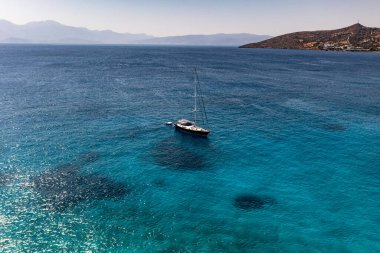 Deniz ve dağların panoramik görüntüsü ve bir drondan çekilen turkuaz su üzerindeki gemiler.