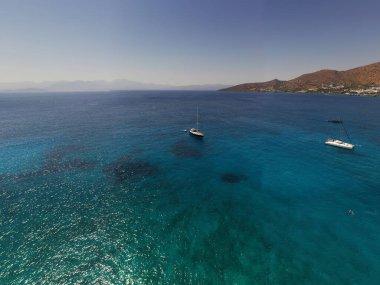 Deniz ve dağların panoramik görüntüsü ve bir drondan çekilen turkuaz su üzerindeki gemiler.
