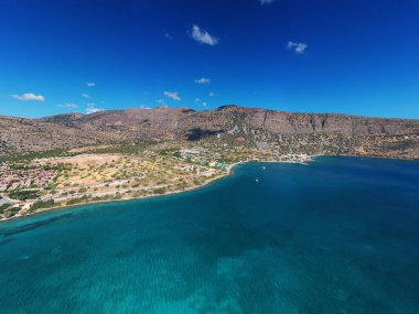 Deniz ve dağların panoramik görüntüsü ve bir drondan çekilen turkuaz su üzerindeki gemiler.