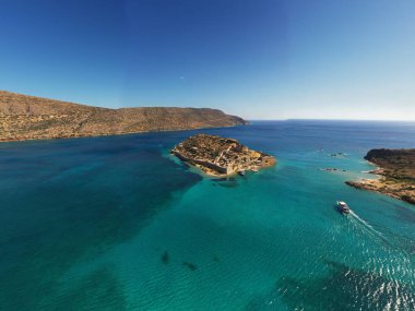 Deniz ve dağların panoramik görüntüsü ve bir drondan çekilen turkuaz su üzerindeki gemiler.