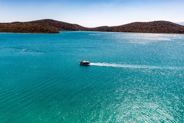 Deniz ve dağların panoramik görüntüsü ve bir drondan çekilen turkuaz su üzerindeki gemiler.