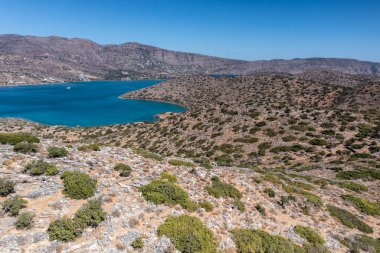 Deniz ve dağların panoramik görüntüsü ve bir drondan çekilen turkuaz su üzerindeki gemiler.