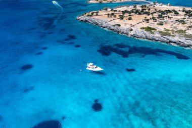 Deniz ve dağların panoramik görüntüsü ve bir drondan çekilen turkuaz su üzerindeki gemiler.