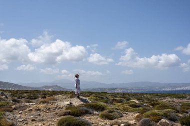 Denizin arka planındaki beyaz elbiseli kadın mavi gökyüzü ve Girit adasındaki antik binalar. 