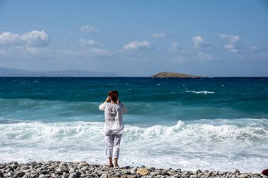 Denizin arka planındaki beyaz elbiseli kadın mavi gökyüzü ve Girit adasındaki antik binalar. 