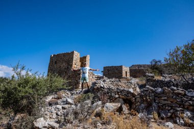 Yeşil giyen bir adam Girit adasındaki eski harap değirmenlerin arka planına karşı. 
