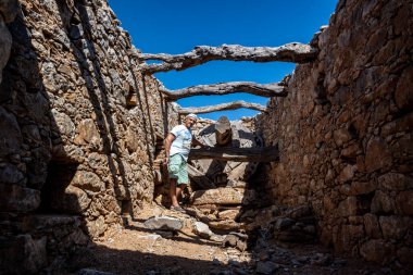 Yeşil giyen bir adam Girit adasındaki eski harap değirmenlerin arka planına karşı. 