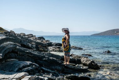 Beyaz şapkalı kadın denizin arka planında taşların üzerinde poz veriyor. 