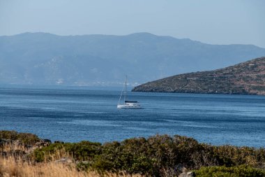 Deniz kıyısına bakan manzara ve ufukta bir deniz gemisi.