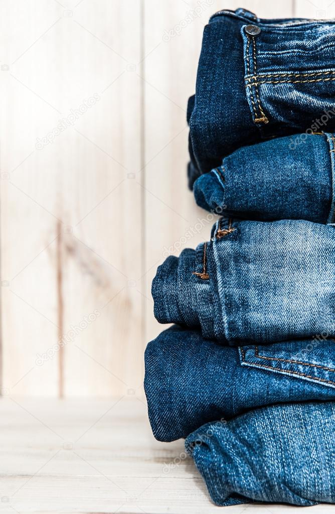 stack of various shades  blue jeans on wooden background