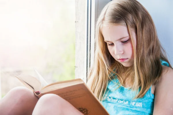 Mignon écolière lecture tout en étant assis sur la fenêtre — Photo