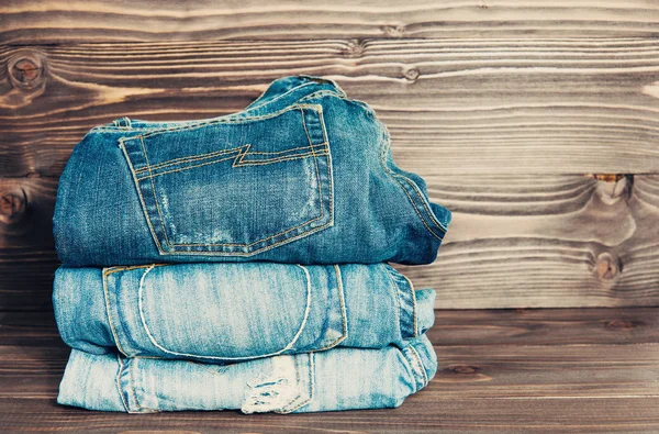 Jeans empilhados em um fundo de madeira, vintage tonificado — Fotografia de Stock