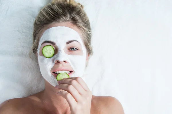 Young woman with facial mask, biting on a cucumber — Stock Photo, Image