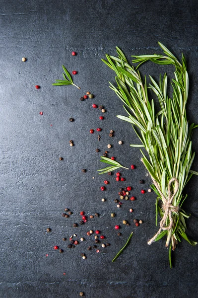 Rosemary orgânico fresco e pimenta na placa de pedra escura — Fotografia de Stock