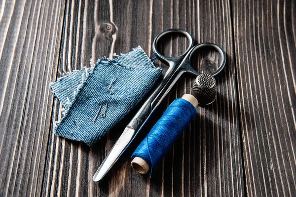 Jeans, hilo azul, aguja y tijera sobre fondo de madera tono oscuro — Foto de Stock