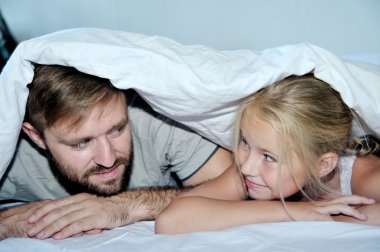 Baba ve kızı eğleniyor gülümseyen bir yatakta yatarken