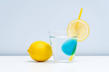 Bir bardak limonata ve beyaz masada taze bir limon.