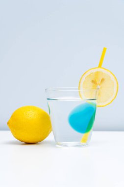 Bir bardak limonata ve beyaz masada taze bir limon.