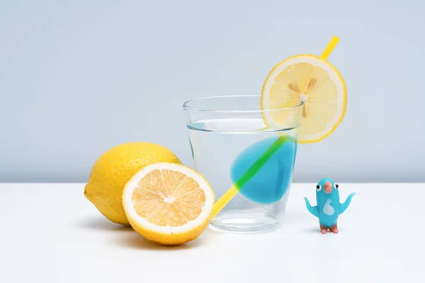 ガラスの中に健康的なレモネードが置かれています 純粋な水とレモンのガラスが白いテーブルの上に置かれている テーブルの上のレモネードとグラスペンギン — ストック写真