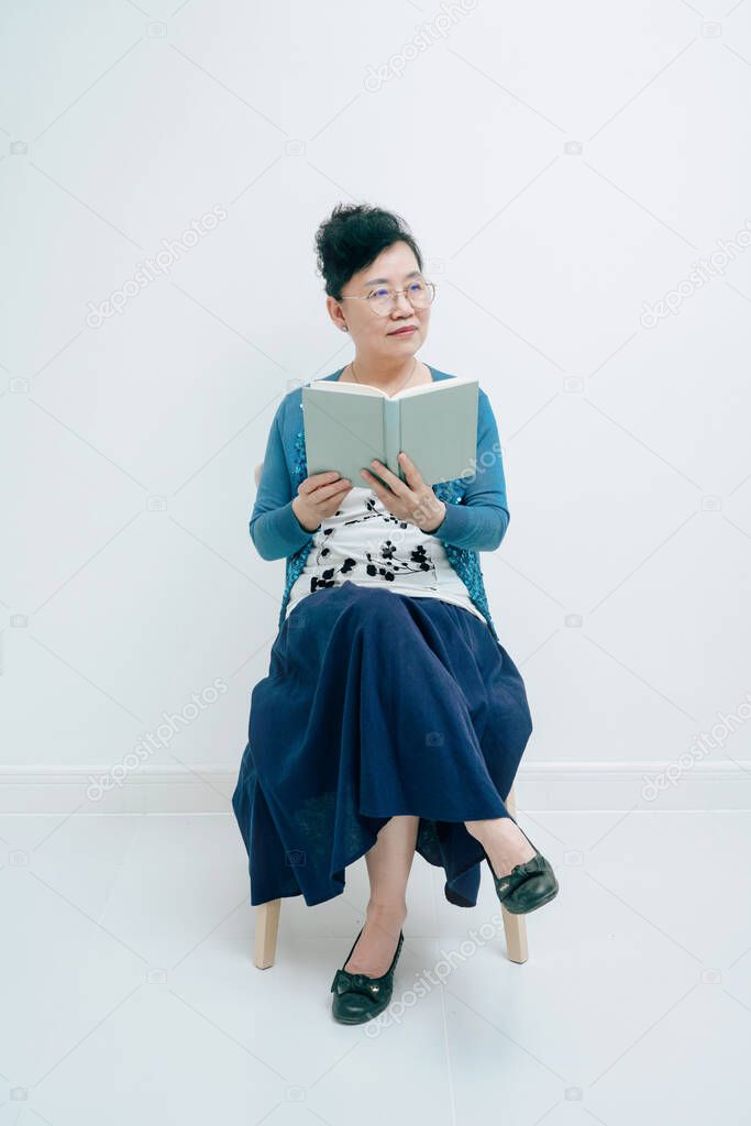 Middle-aged lady reading a book while sitting in front of white background