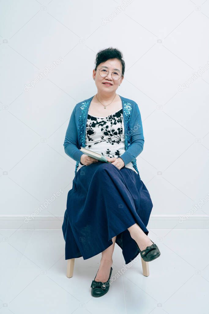 Middle-aged lady sitting on white background holding a book in hand