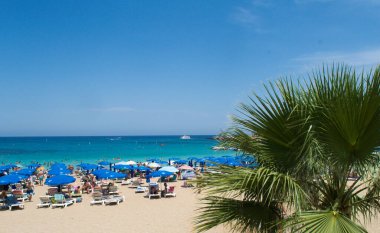 PROTARAS, CYPRUS - 16 Haziran 2018 'de Kıbrıs Rum Kesimi' nin Protaras kentinde güneşli bir günde yerel belediye plajı insanlarla dolup taşıyor. 