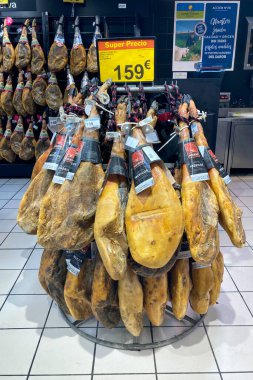 TORREMOLINOS, SPAIN - 1 Aralık 2025: İspanya 'nın Torremolinos kentindeki Carrefour' da Noel öncesi geniş bir jamon koleksiyonu gösteriliyor ve bayram sezonu için geleneksel İspanyol pişirilmiş etleri sergileniyor.