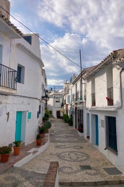 FRIGILIANA, SPAIN - 10 Mayıs 2025: Frigiliana, İspanya 'da beyazlatılmış evler ve renkli çiçeklerle çevrili büyüleyici dar sokaklarda huzurlu bir yürüyüş