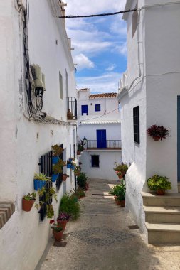 FRIGILIANA, SPAIN - 10 Mayıs 2025: Frigiliana, İspanya 'da beyazlatılmış evler ve renkli çiçeklerle çevrili büyüleyici dar sokaklarda huzurlu bir yürüyüş