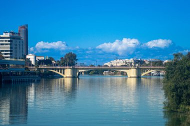 SEVILLA, İspanya - 25 Aralık 2025: Guadalquivir Nehri 'nin panoramik bir görüntüsü, Sevilla, İspanya' da çağdaş bir şehir manzarasını şekillendirerek, liman boyunca modern mimariyi yansıtır..