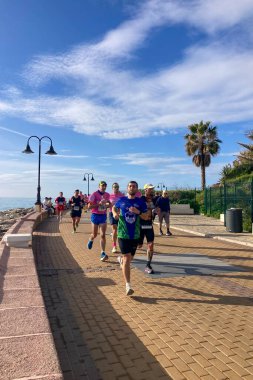 TORREMOLINOS, SPAIN - FEBRUARY 12026: Koşucular, İspanya 'nın Torremolinos kentinin güneşli zeminine karşı dayanıklılık ve enerji sergileyerek kıyı caddelerinde yarı maraton koşuyorlar.