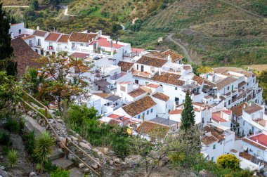 FRIGILIANA, SPAIN - 10 Mayıs 2025: Frigiliana, İspanya 'da beyazlatılmış evler ve renkli çiçeklerle çevrili büyüleyici dar sokaklarda huzurlu bir yürüyüş