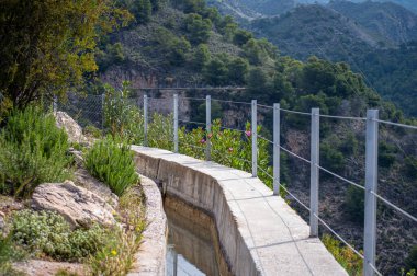 İspanya 'nın Frigiliana kentindeki eski bir sulama hendeği boyunca bir yürüyüş yolundan çevresindeki dağların ve resimli köyün manzarası..