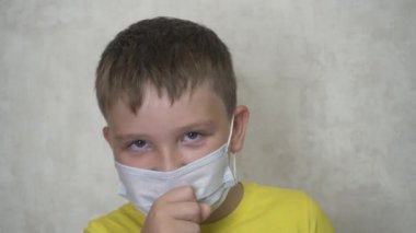 Sarı tişörtlü ve tıbbi maskeli bir çocuk öksürüyor.
