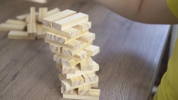 O menino na mesa constrói uma torre de dominós de madeira close-up — Vídeo de Stock