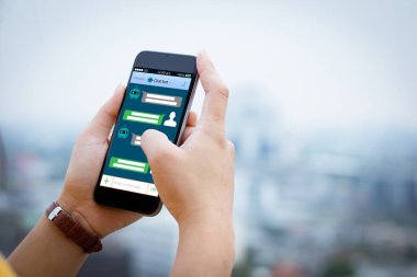 Yapay zeka, yapay zeka, robot sohbeti. Arka plan olarak bulanık şehir üzerinde cep telefonu tutan eller.