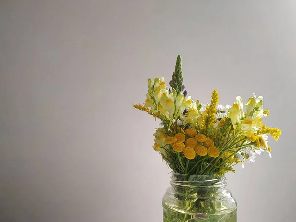 Different wild flowers in a transparent vase on a white background